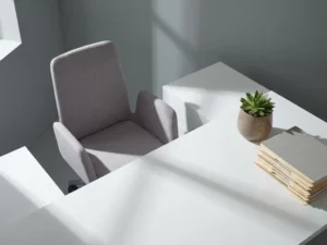 Lege bureaustoel werpt lange schaduw over wit bureau met vetplant en mappen in minimalistisch kantoor